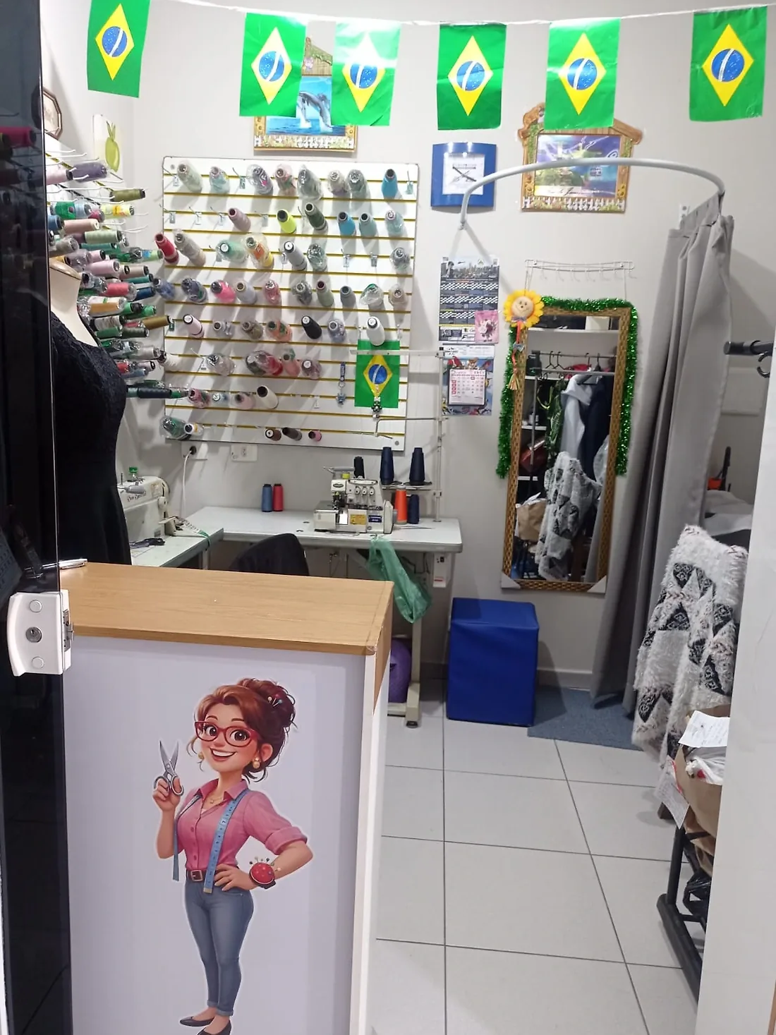 Interior do ateliê: máquinas de costura, linhas e espelho de prova
